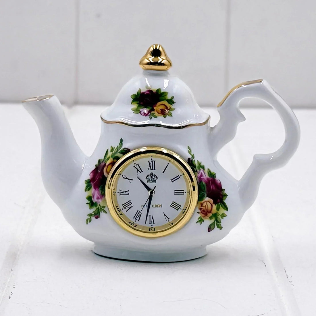Porcelain teapot clock with floral design, gold trim, and Roman numerals for elegant home décor