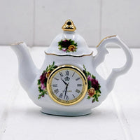 Porcelain teapot clock with floral design, gold trim, and Roman numerals for elegant home décor
