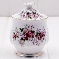 A white Royal Albert Lavender Rose bone china lidded sugar bowl or jam pot decorated with pink roses, green leaves, and gold trim, set against a light background.