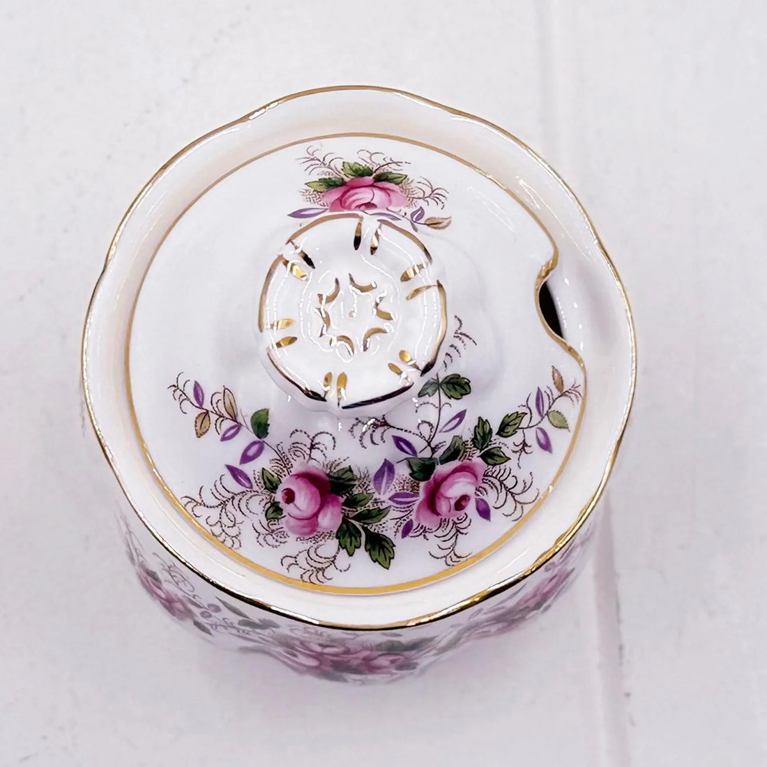 A white Royal Albert  Lavender Rose preserve/sugar/jam pot with a floral design featuring pink roses, green leaves, and gold accents, photographed from a top-down angle on a light textured background.