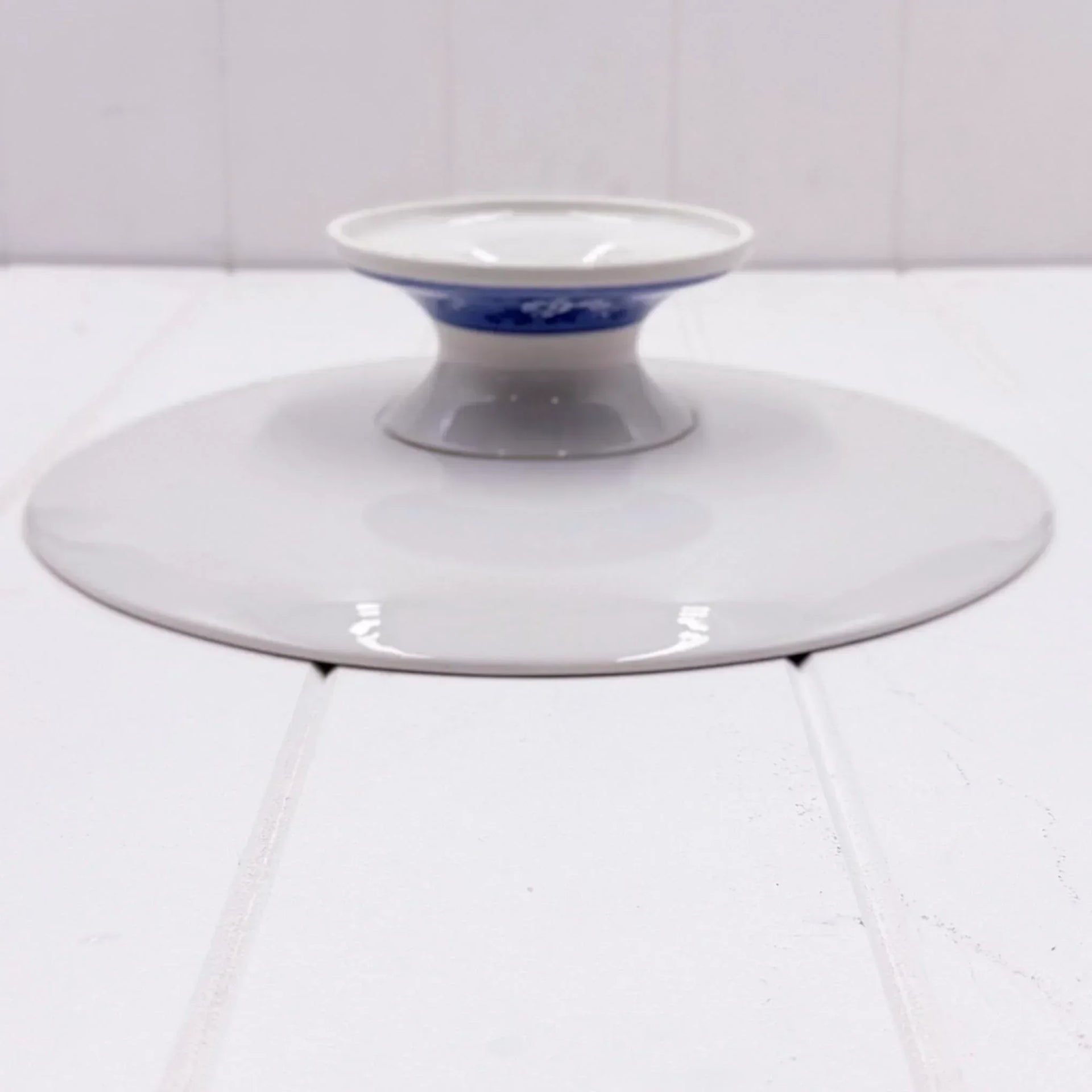 White ceramic pedestal dish with blue floral band, elegant home décor accent on white surface