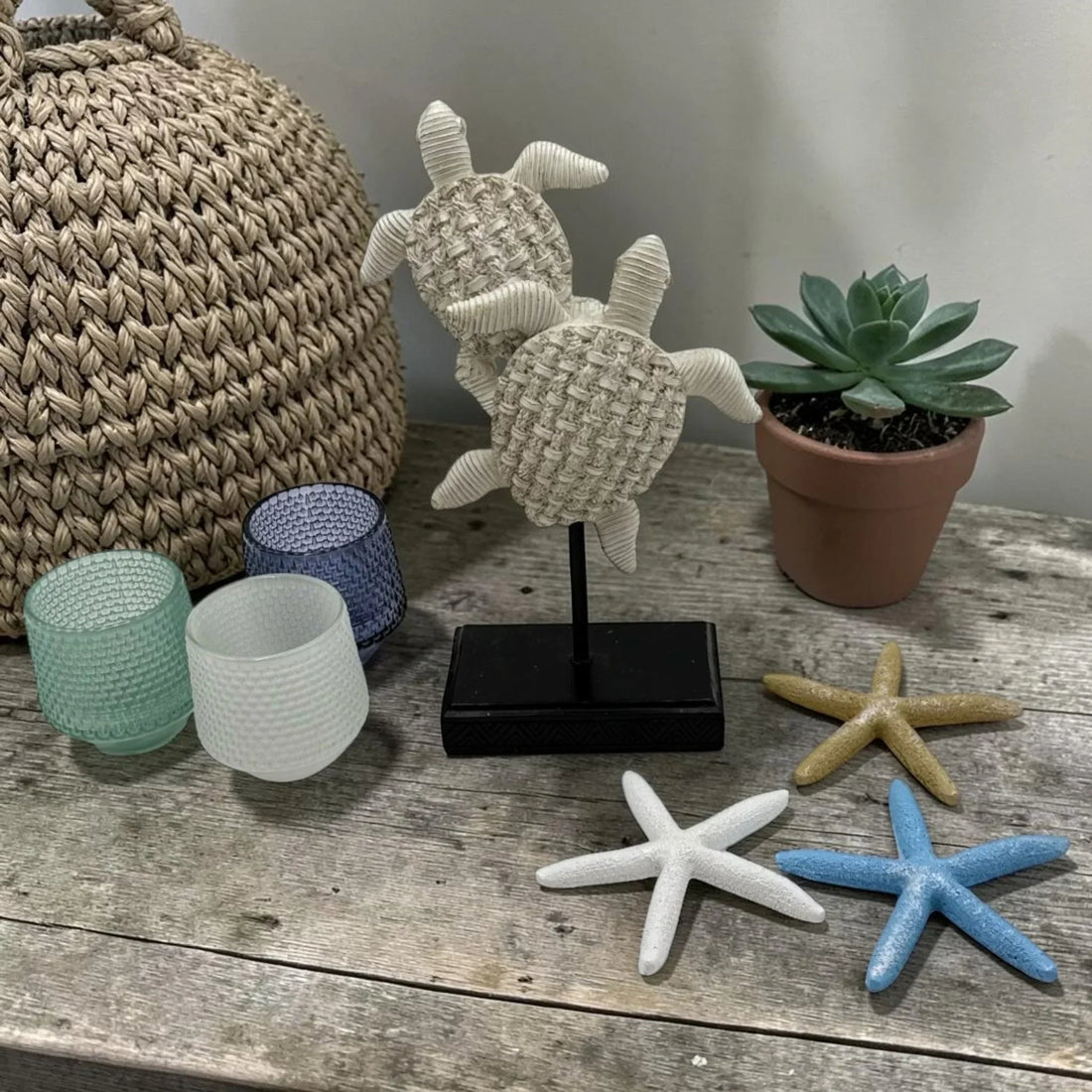 Coastal home décor with woven turtle sculpture, starfish, succulent, and textured glass candle holders on rustic wood.