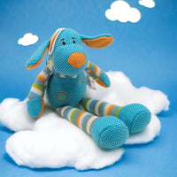 Knitted blue bunny plush toy with striped limbs, sitting on white cloud against blue sky background