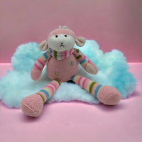 Knitted pink monkey toy with rainbow stripes, sitting on fluffy cloud against pink background