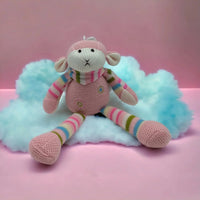 Knitted pink monkey toy with rainbow stripes, sitting on fluffy cloud against pink background