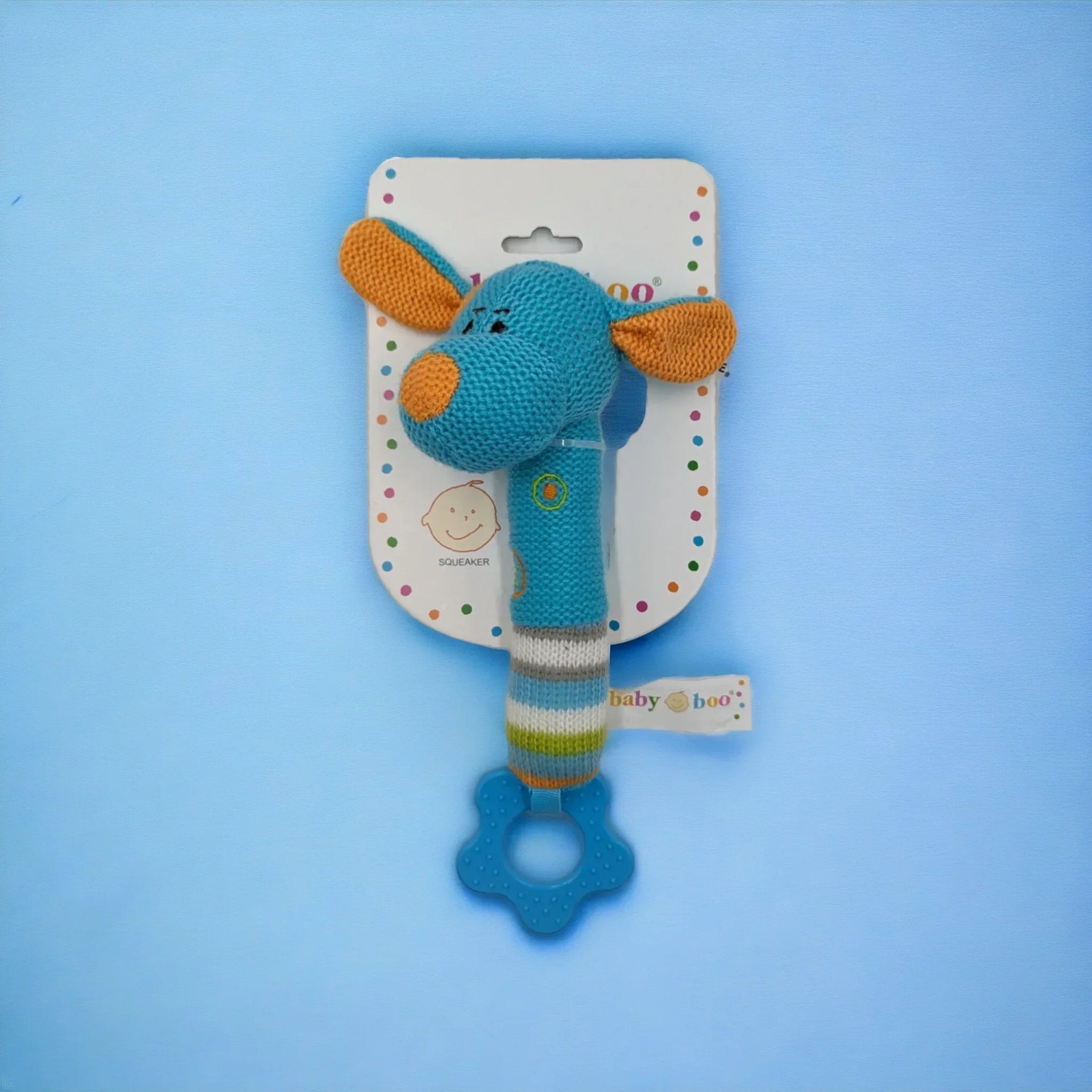 Blue knitted giraffe baby rattle with teether, squeaker, and striped handle on packaging