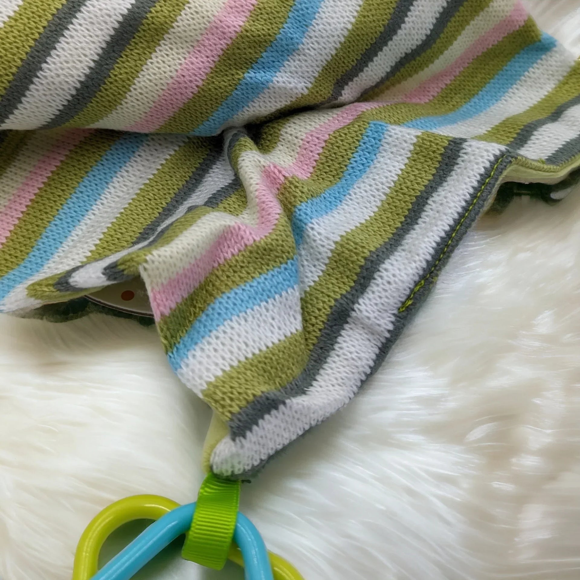 Striped baby blanket with pastel colors and attached teething rings on fluffy white surface