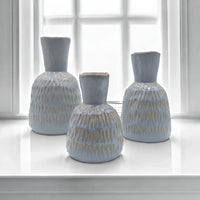 Set of three light blue textured ceramic vases on white windowsill, modern home decor accents