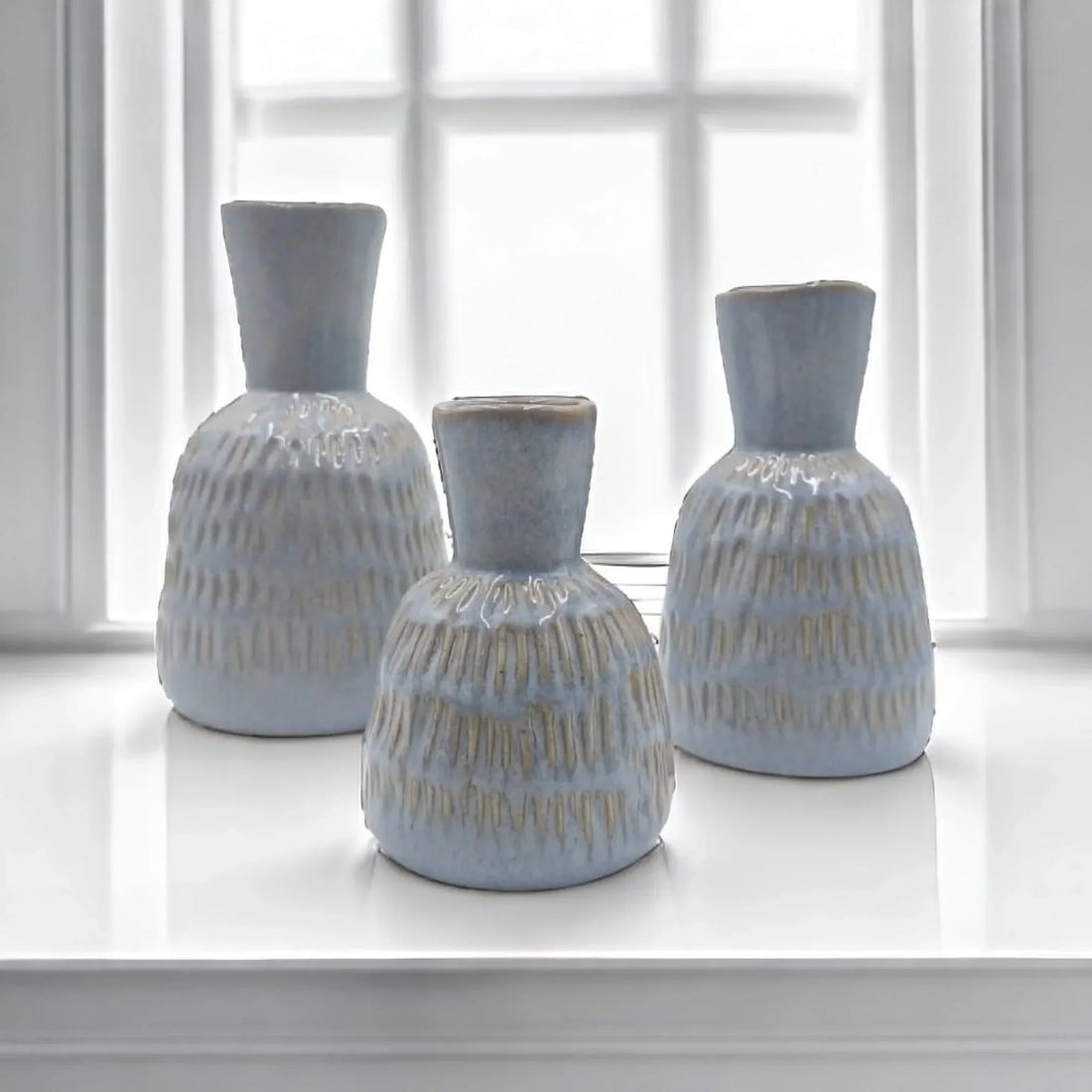 Set of three light blue textured ceramic vases on white windowsill, modern home decor accents