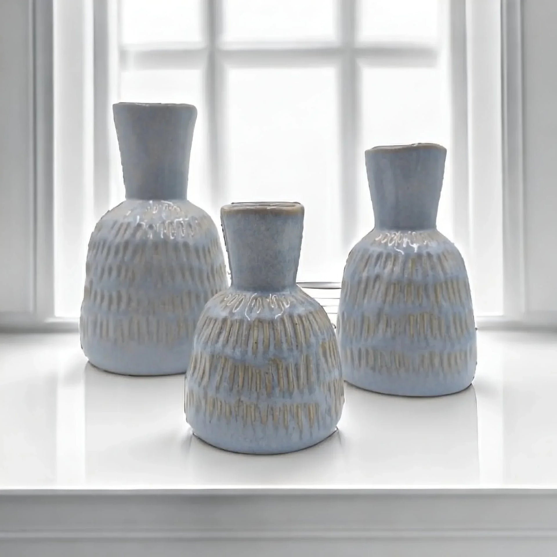 Set of three light blue textured ceramic vases on white windowsill, modern home decor accents