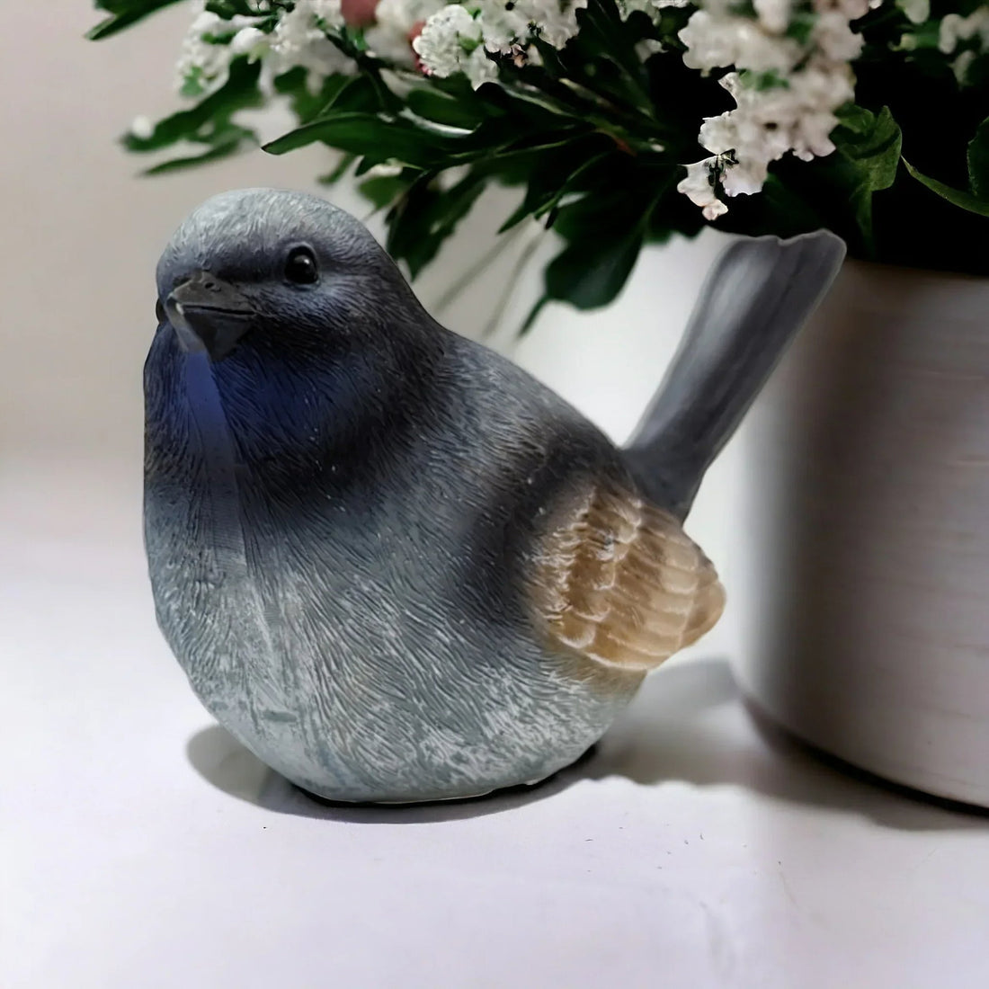 Grey ceramic bird figurine with blue chest, home décor accent near white flowers