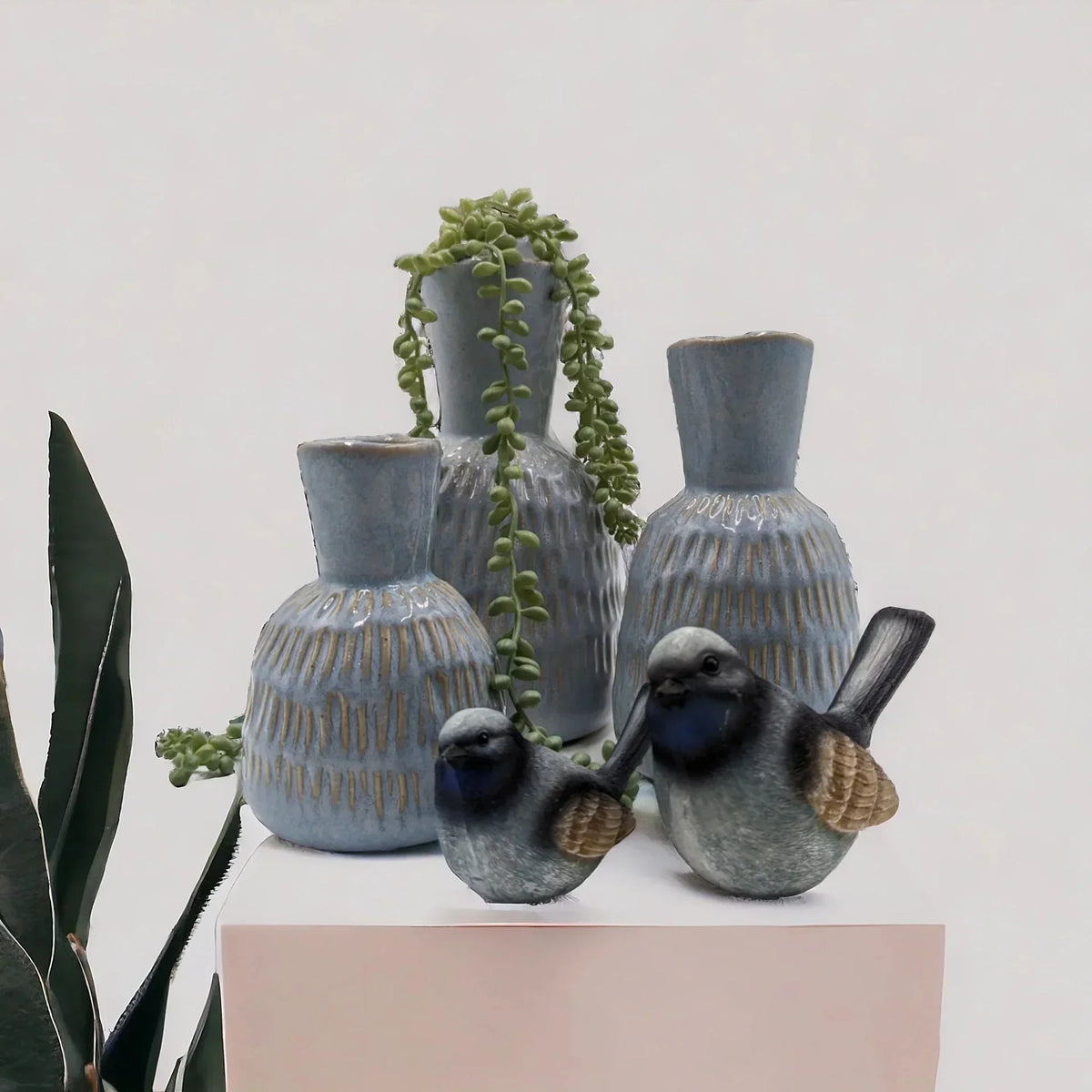 Ceramic bird figurines with blue-grey glaze beside textured vases and trailing succulent, home décor accent pieces