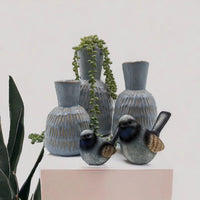 Ceramic bird figurines with blue-grey glaze beside textured vases and trailing succulent, home décor accent pieces