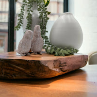 Two textured bird figurines on rustic wood slab with greenery and white vase, home décor accent