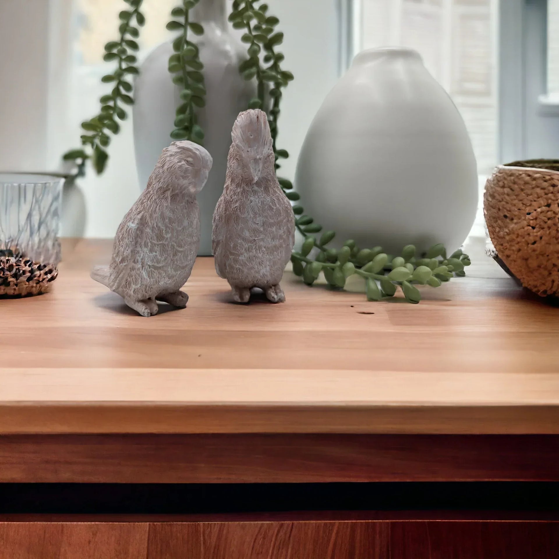 Set of two textured bird figurines on wooden shelf with greenery and ceramic vases, home décor accent