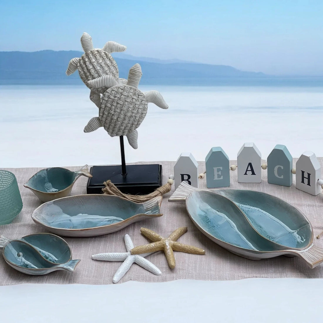 Coastal home décor with ceramic fish bowls, starfish, turtle sculpture, and 'BEACH' sign for seaside styling