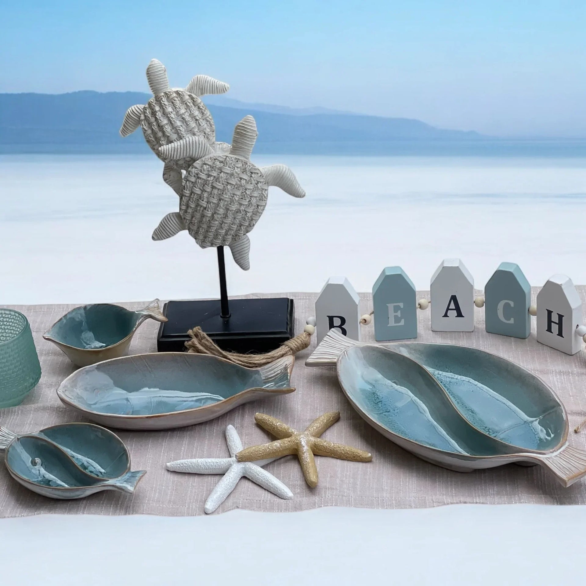 Coastal home décor with ceramic fish bowls, starfish, turtle sculpture, and 'BEACH' sign for seaside styling