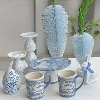 Blue and white ceramic mugs, egg, plate, candlesticks, and bunny decor with feather accents for elegant home styling