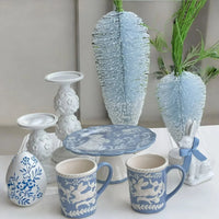 Blue and white ceramic mugs, egg, plate, candlesticks, and bunny decor with feather accents for elegant home styling