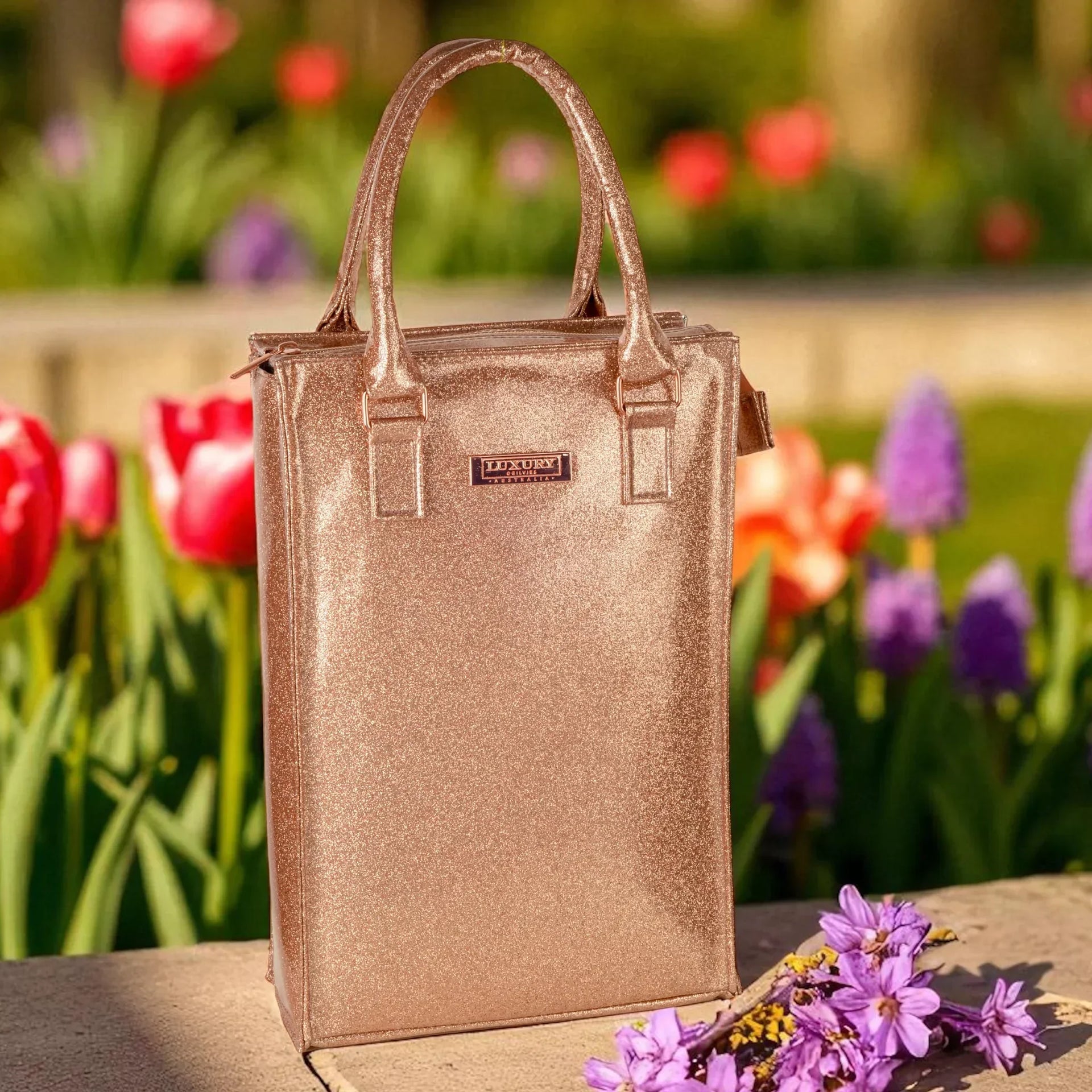 Sparkling rose gold tote bag with 'Luxury Australia' plaque, set against vibrant garden blooms for elegant home décor.