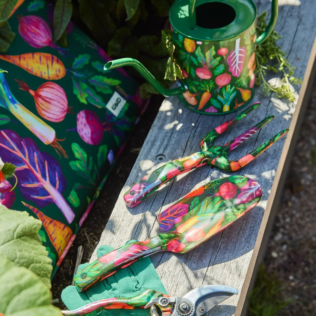 Colorful vegetable-patterned gardening tools and watering can on rustic wood