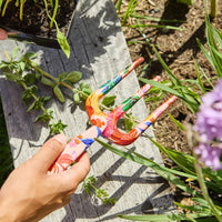 Colorful floral garden fork for planting, held over wooden bench with greenery and purple flowers