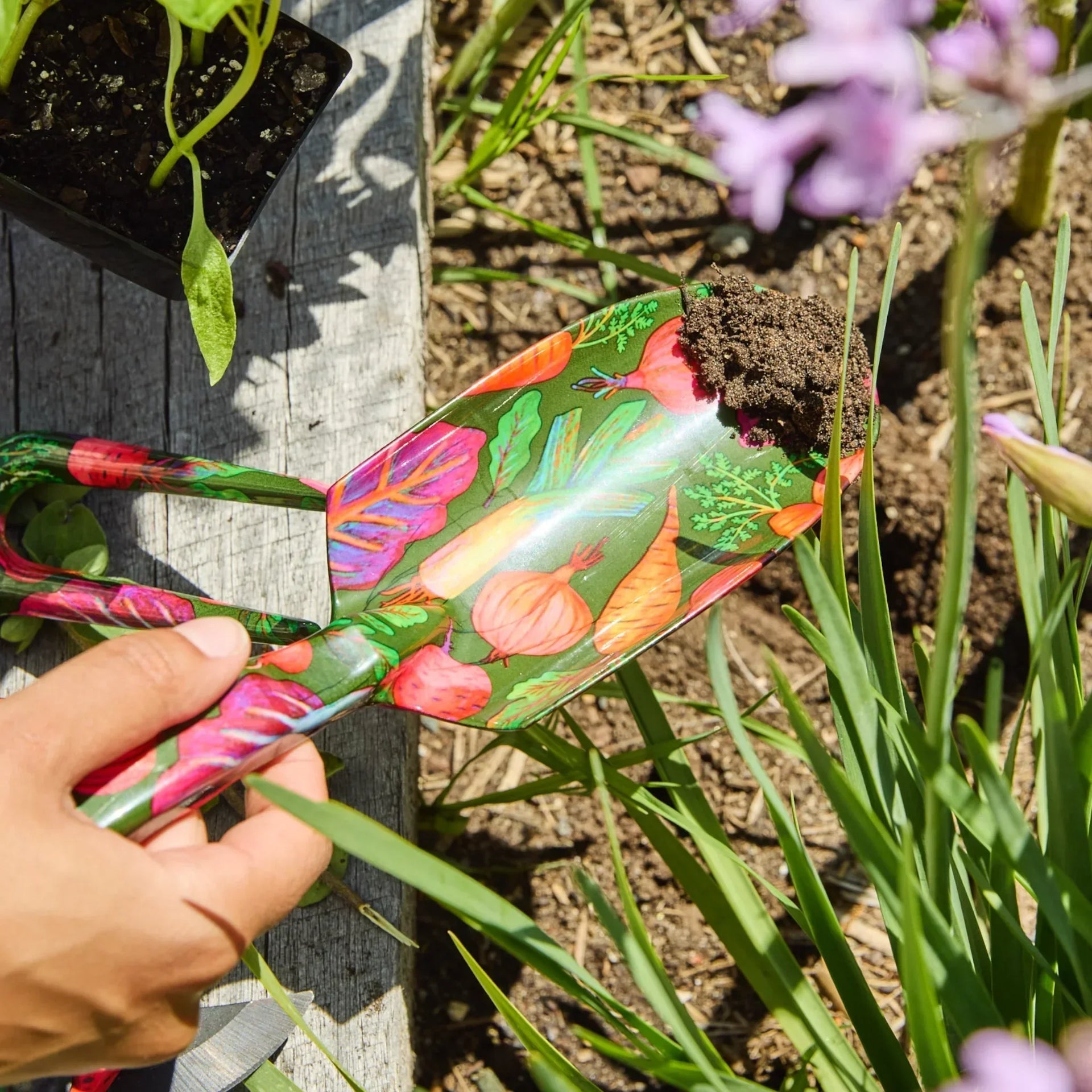 Colorful vegetable-patterned garden trowel scooping soil in a vibrant garden setting
