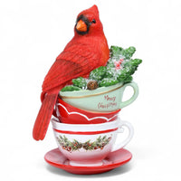 Red cardinal perched on stacked Christmas teacups with festive greenery and 'Merry Christmas' text