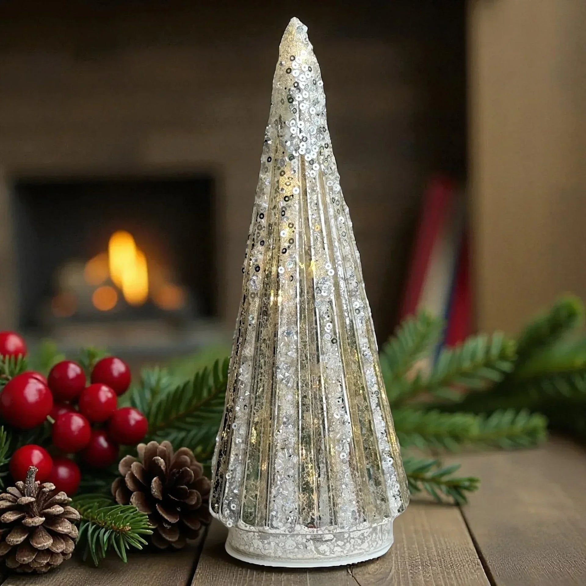 Sparkling silver sequin Christmas tree decoration with warm fireplace background, festive pine and berries