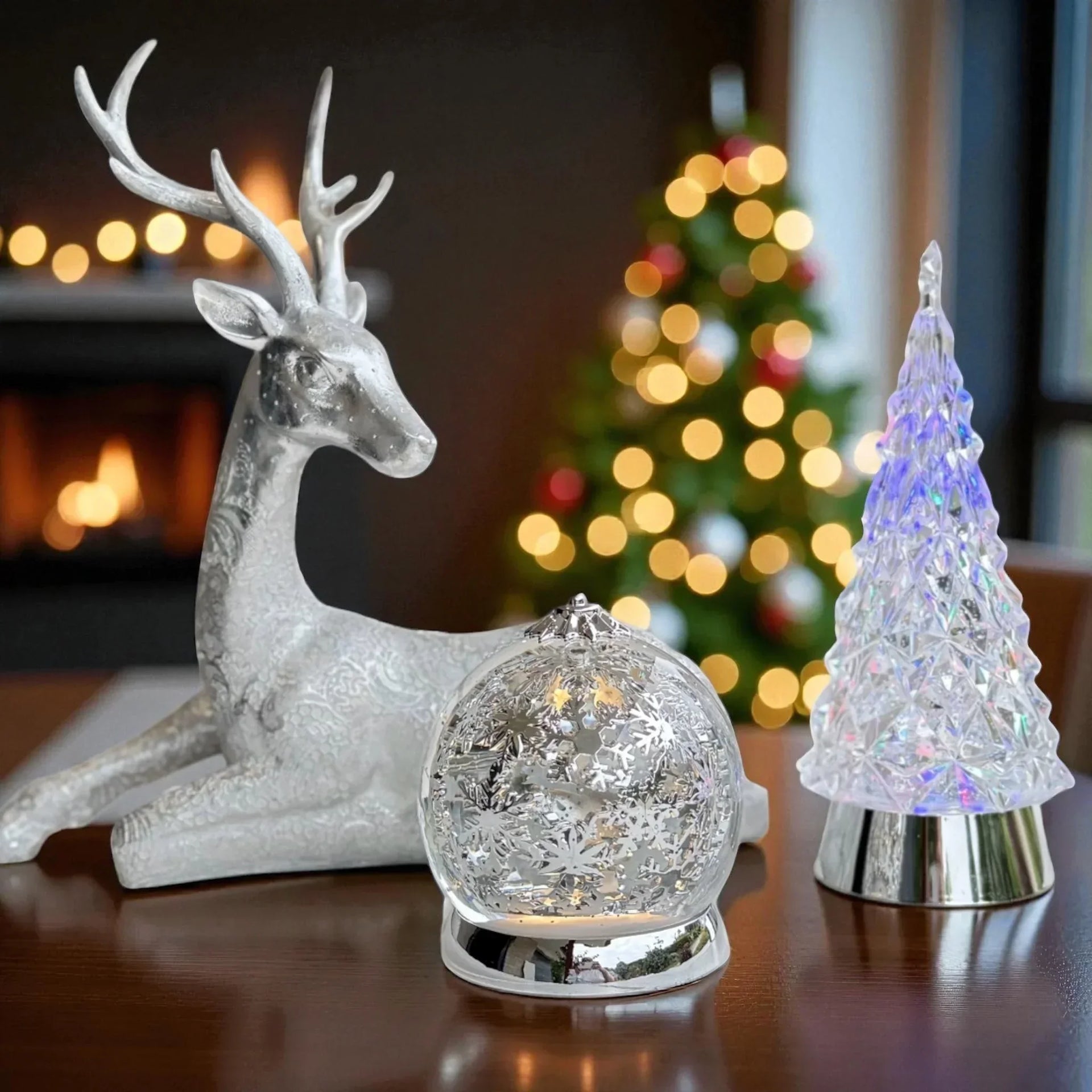 Silver reindeer, snow globe, and crystal Christmas tree decor with festive lights and fireplace background