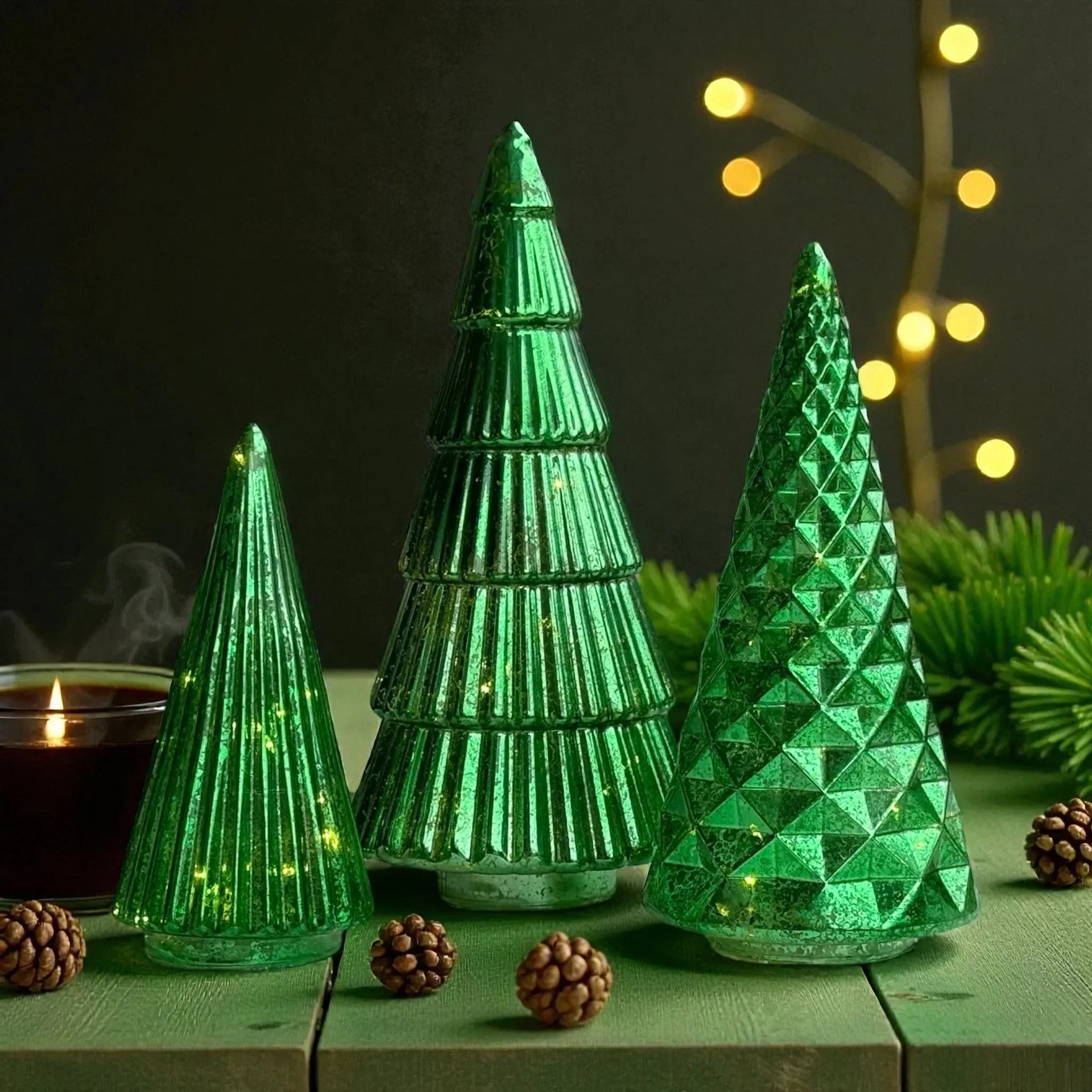 Green glass Christmas tree decorations with LED lights, pinecones, and candle on rustic table