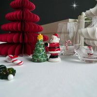 Ceramic Santa figurine beside mini Christmas tree, candy canes, and glassware for festive holiday decor