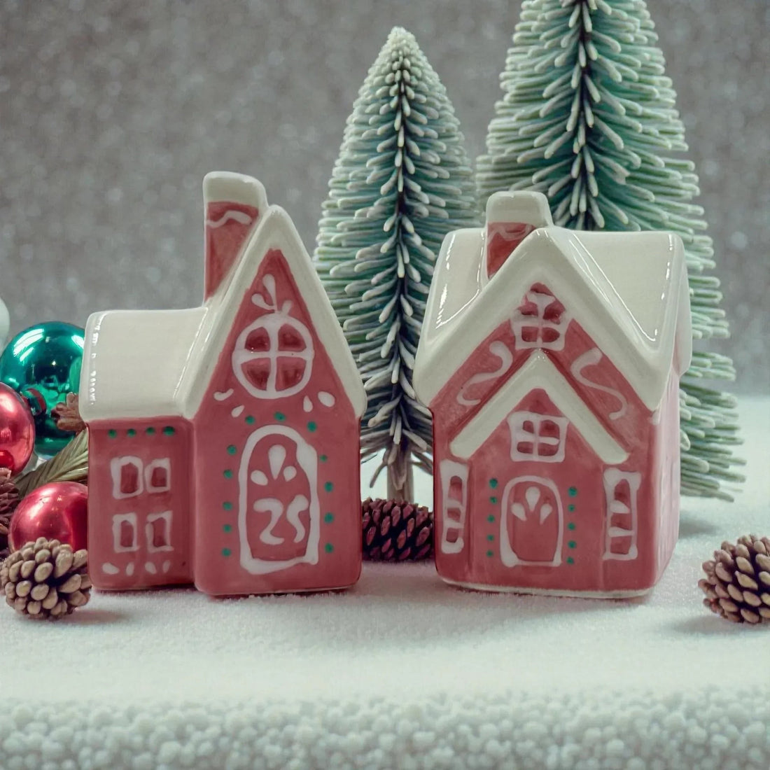 Pink ceramic gingerbread houses with white roofs, festive ornaments, and snowy pine trees for holiday home décor