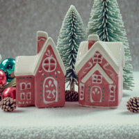 Pink ceramic gingerbread houses with white roofs, festive ornaments, and snowy pine trees for holiday home décor