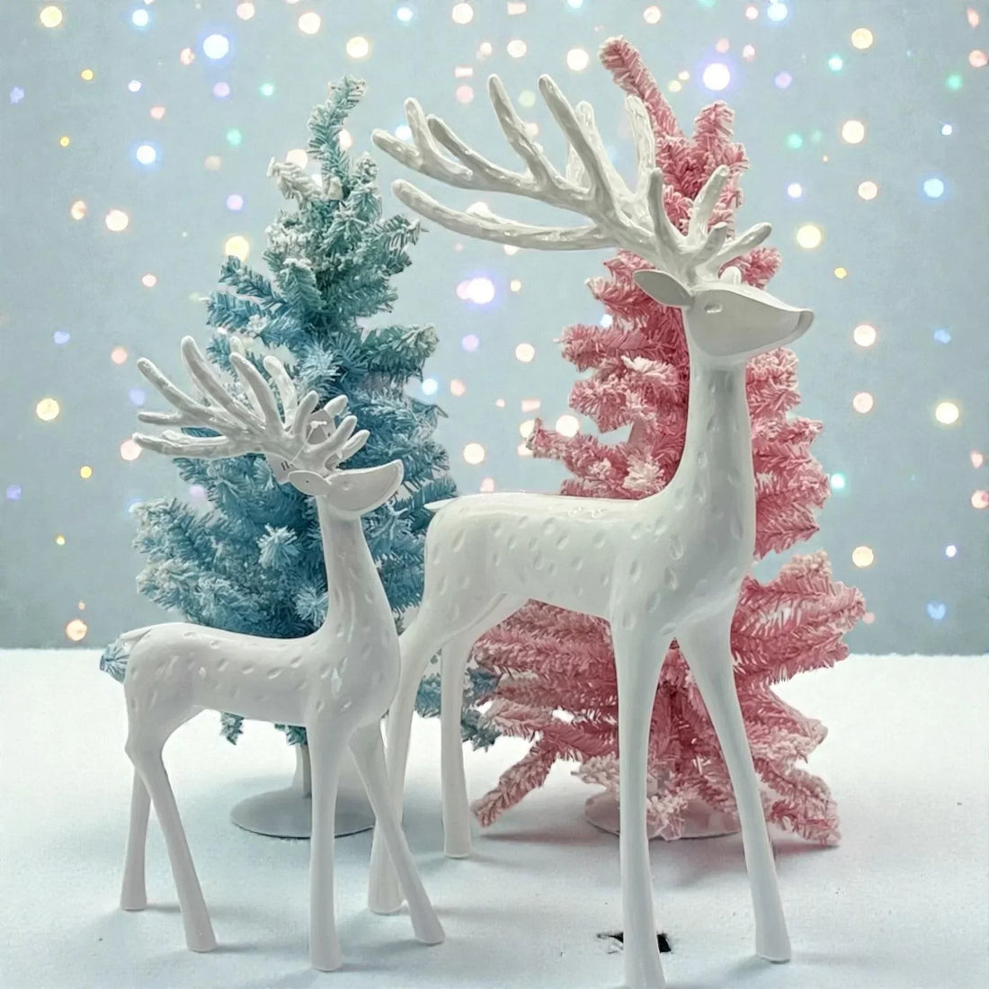 White ceramic reindeer figurines with pastel blue and pink Christmas trees, festive holiday decor