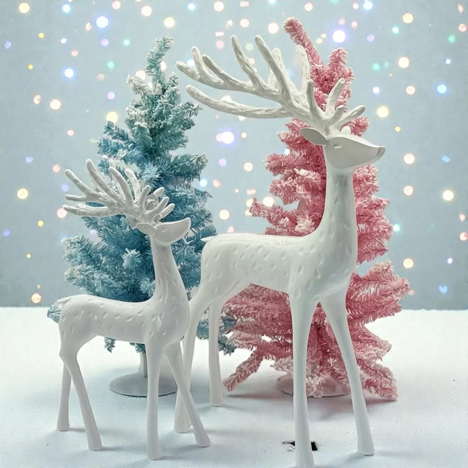 White ceramic reindeer figurines with pastel blue and pink Christmas trees, festive holiday decor