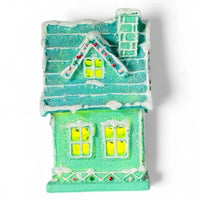 Miniature teal Christmas house with glowing windows, snow-dusted roof, and festive lights for holiday home décor