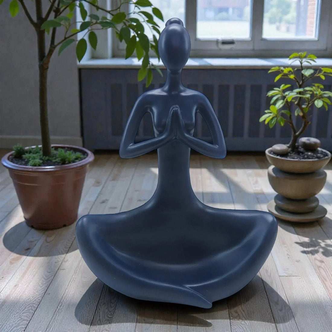 Sleek gray meditating figure sculpture for modern home décor, styled with potted plants on wood floor