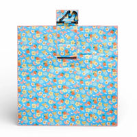 Blue picnic blanket with fruit & flower print, pink trim, and carry strap for outdoor use