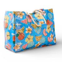 Blue tropical tote bag with fruit, flowers, shells, and rope handles for beach or market use