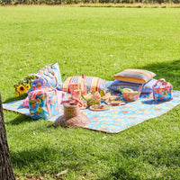 Colorful picnic setup with floral blanket, striped cushions, and vintage-style accessories on lush green grass