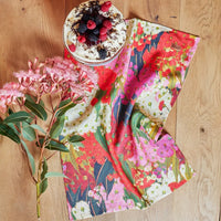 Vibrant floral tea towel with eucalyptus blooms, paired with a berry-topped dessert on wooden table