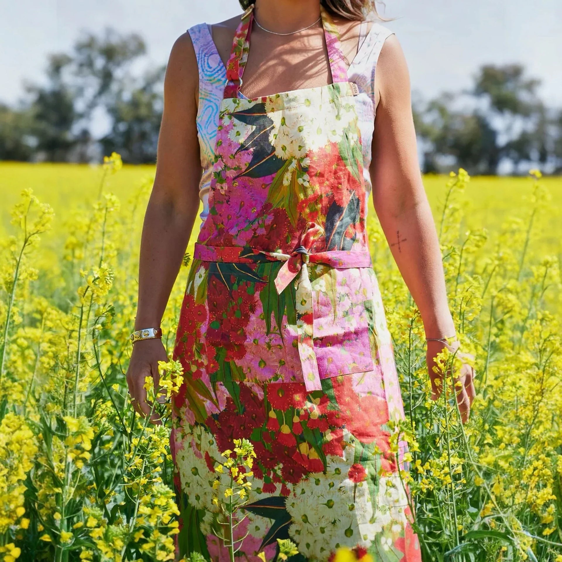 Floral print apron with vibrant pink, red, and white flowers, worn in a sunny yellow field