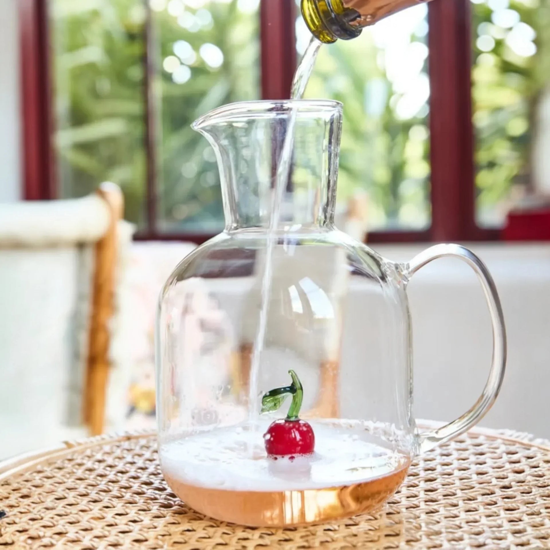 Clear glass pitcher with cherry design, being filled with sparkling wine, perfect for home entertaining and décor