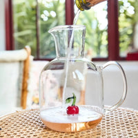 Clear glass pitcher with cherry design, being filled with sparkling wine, perfect for home entertaining and décor