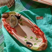 Ceramic seafood platter with lobsters, oysters, mussels, and lemon slices on teal napkin