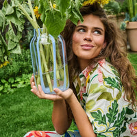 Woman holding glass vase with sunflowers in garden, floral shirt, home décor