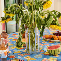 Sunflowers in glass vase on colorful fruit-print tablecloth with watermelon and wine, home décor styling
