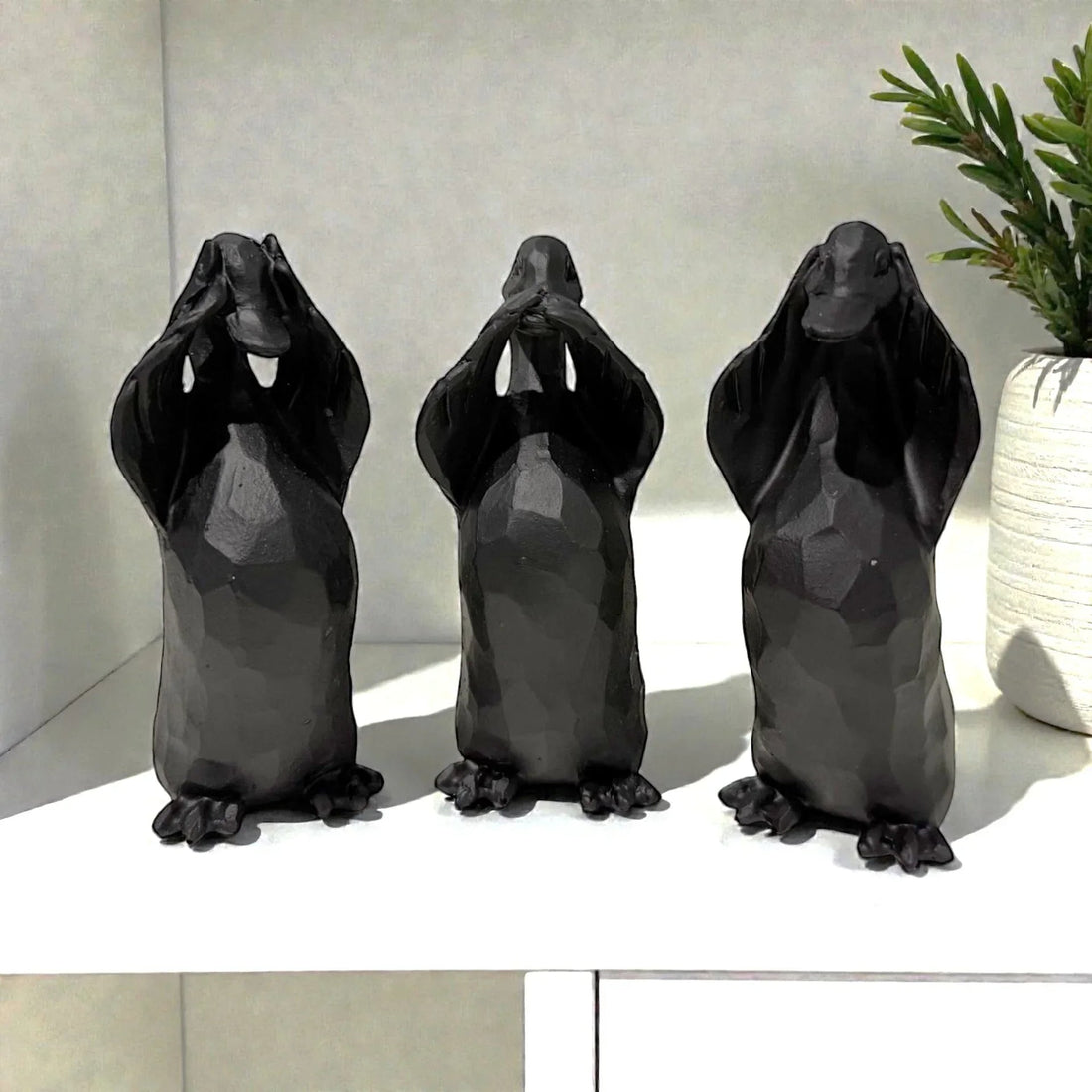 Black ceramic three wise monkeys home decor statues on shelf with green plant