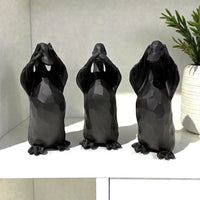 Black ceramic three wise monkeys home decor statues on shelf with green plant